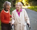 87 years old woman outdoors with the help of a walker and her mature daughter
