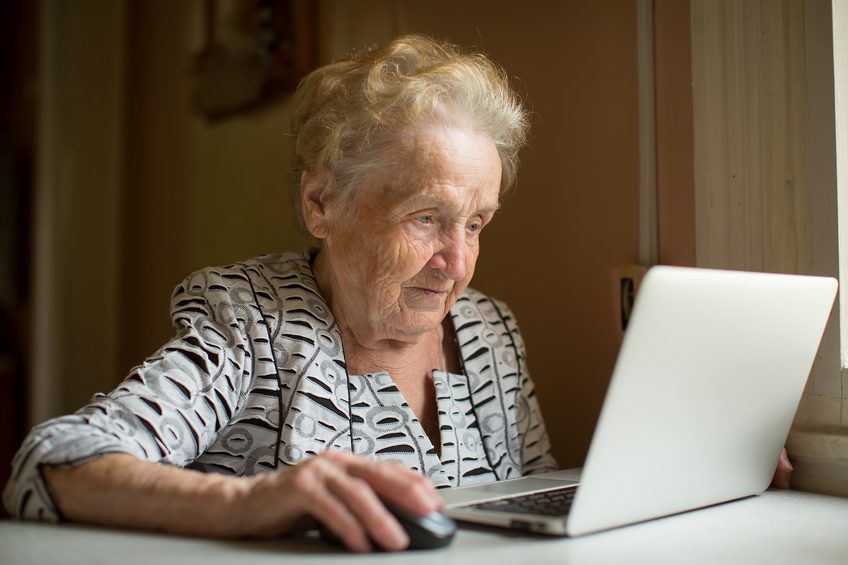 Elderly woman working on laptop sitting near the window.