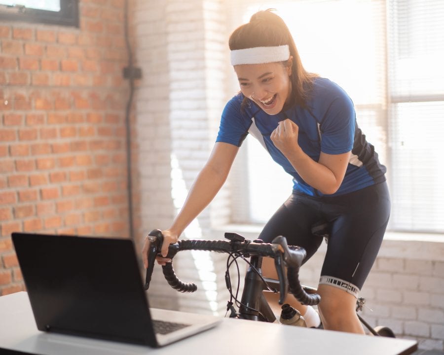 Asian woman cyclist. She is exercising in the house. By cycling on the trainer And playing online bike games, she is glad to succeed.