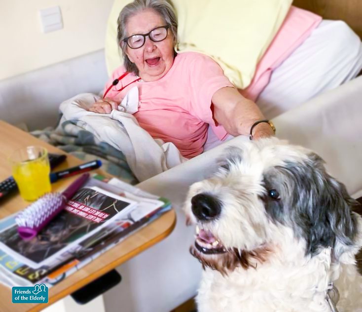 A resident from The Old Vicarage care home smiling and petting MJ the dog.