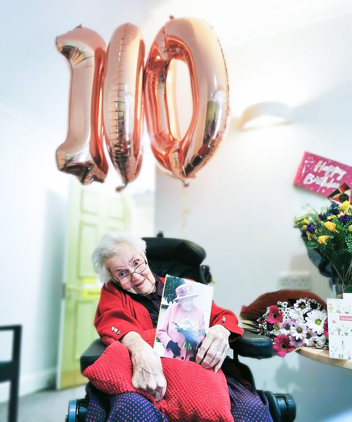 Moyra celebrating her 100th Birthday with balloons, presents and a card from The Queen. 