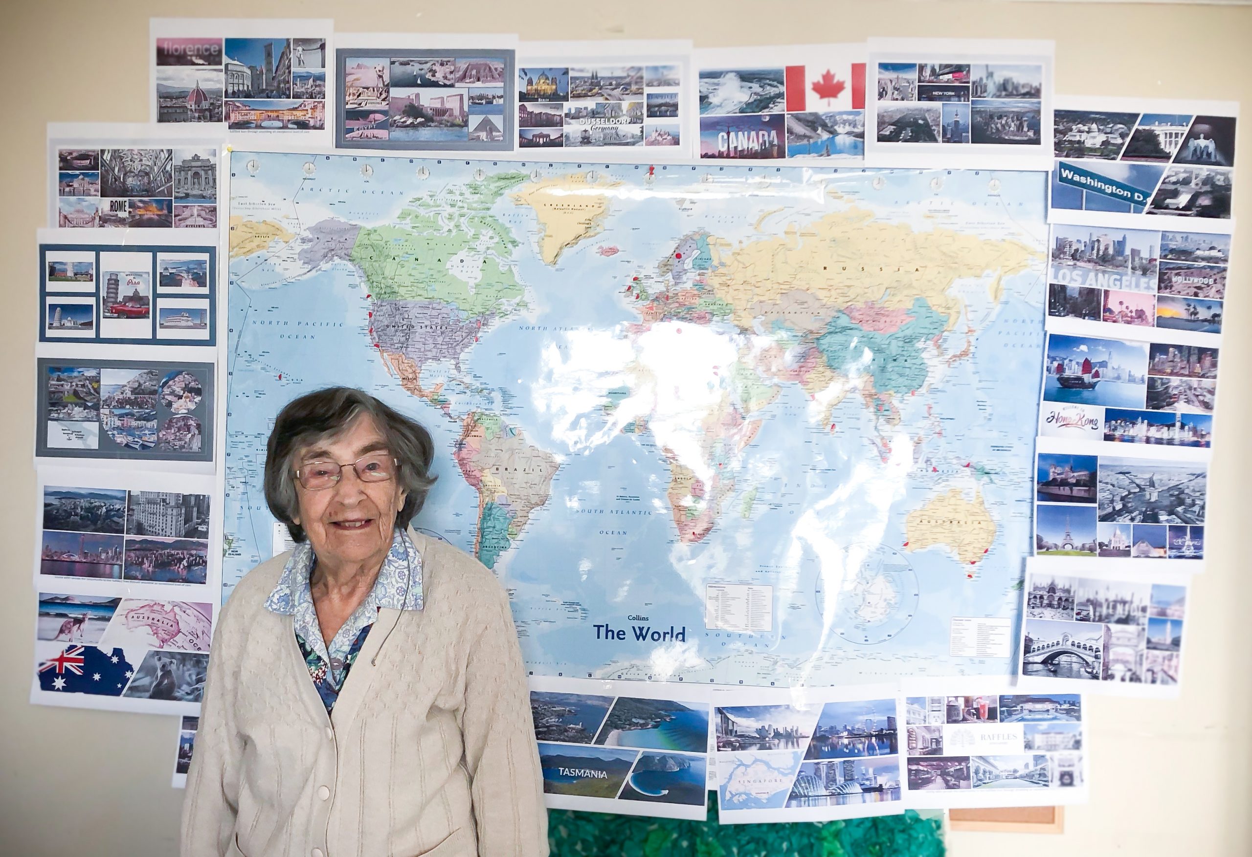 Evelyn standing in front of a world map and images of places she and John visited