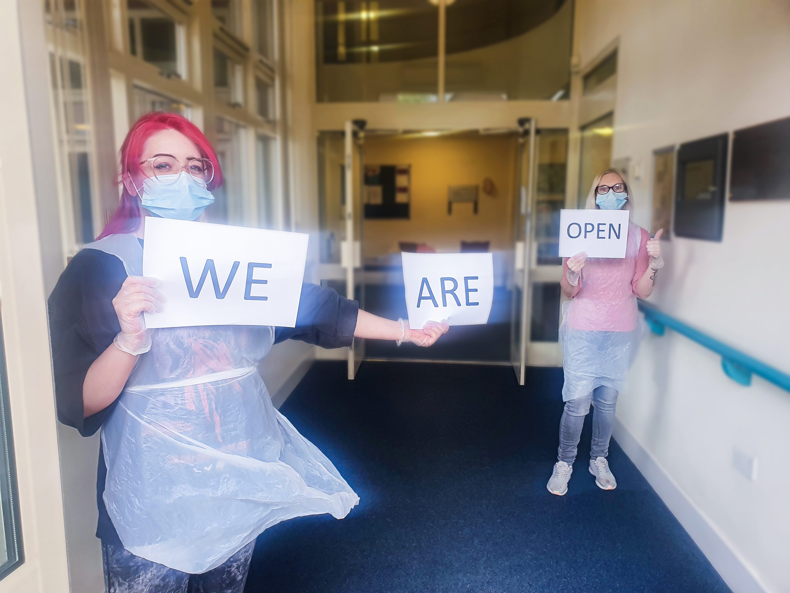 Woking Day Care staff holding a sign saying 'We Are Open'