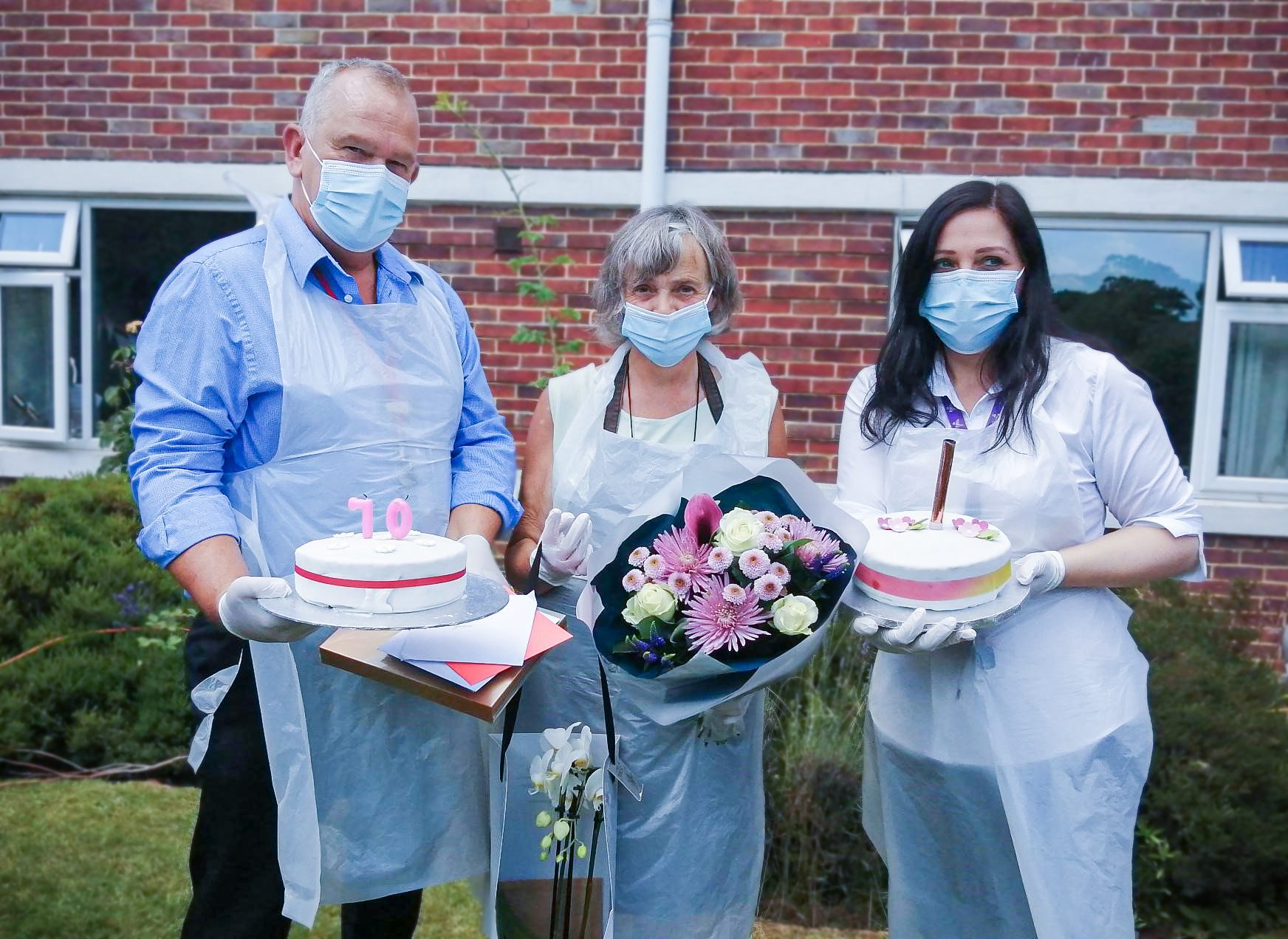 Staff and Grace holding cake and flowers and smiling at the camera.