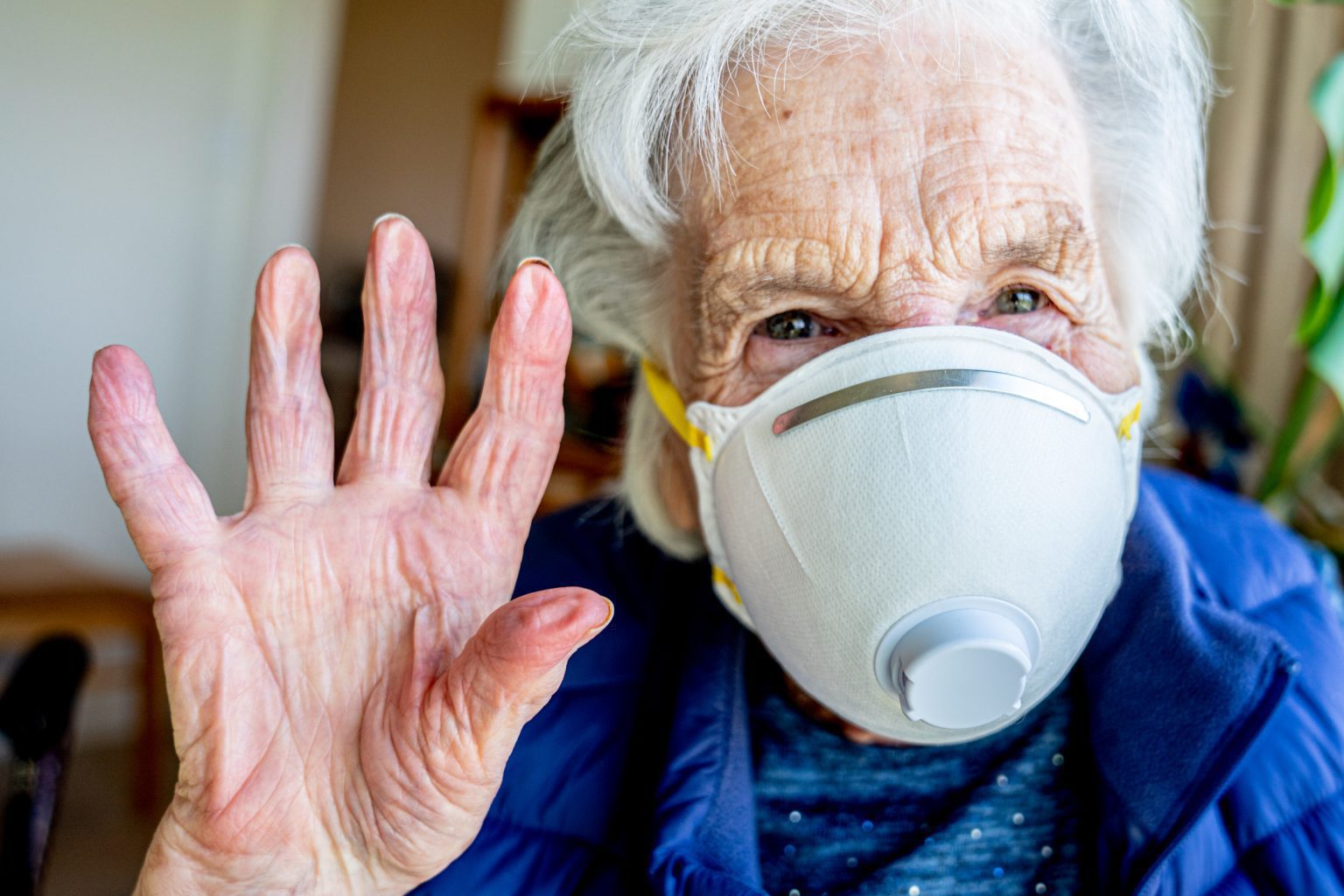 Close-Up Shot of Elderly Senior Caucasian Woman Smiling Holding Her Hands Up Waving Hello or Goodbye Wearing an n95 Protective Face Mask To Prevent the Spread of COVID SARS nCoV 19 Coronavirus Swine Flu H7N9 Influenza Illness During Cold and Flu Season
