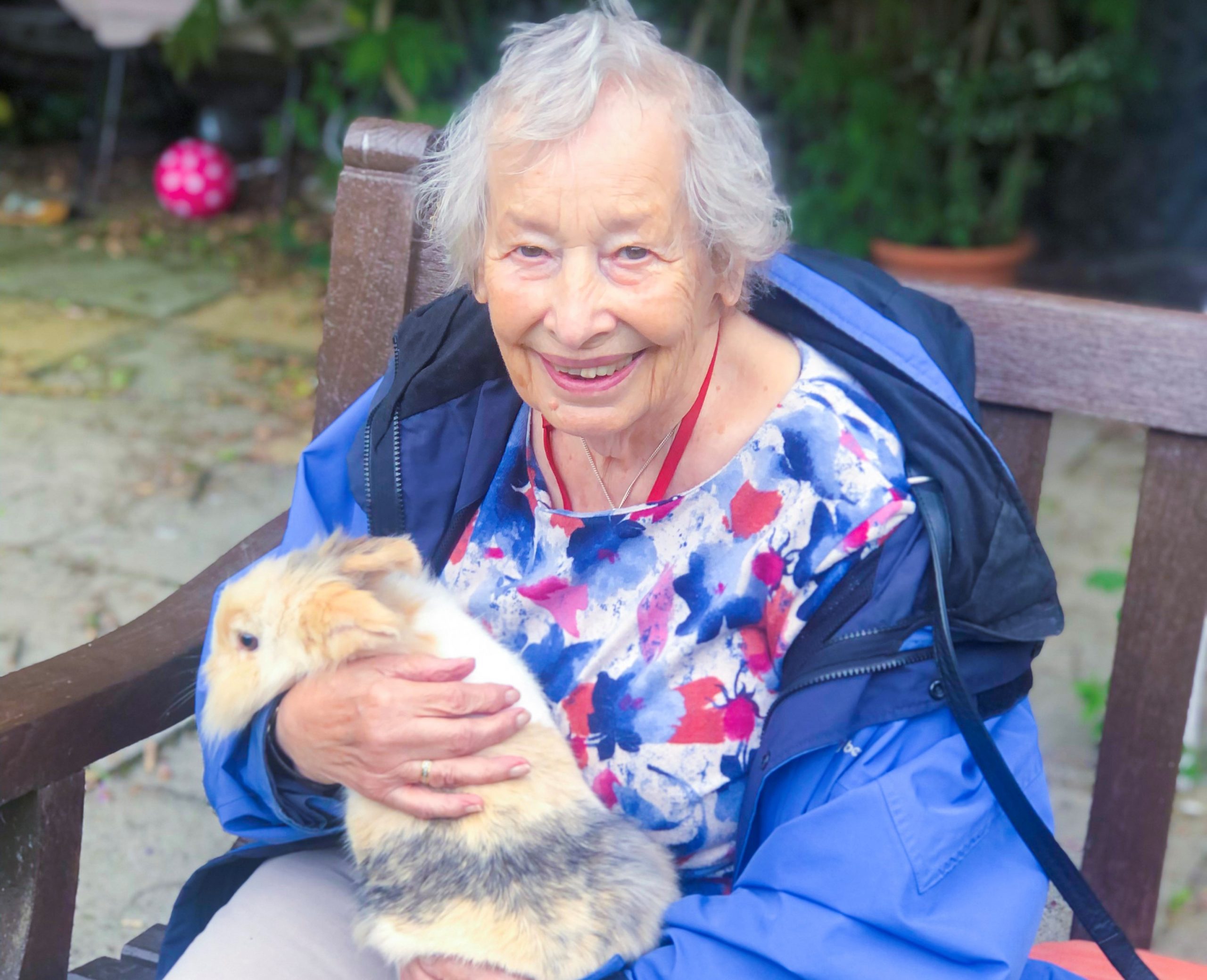 An RNNH care home resident cuddling a rabbit and smiling. 