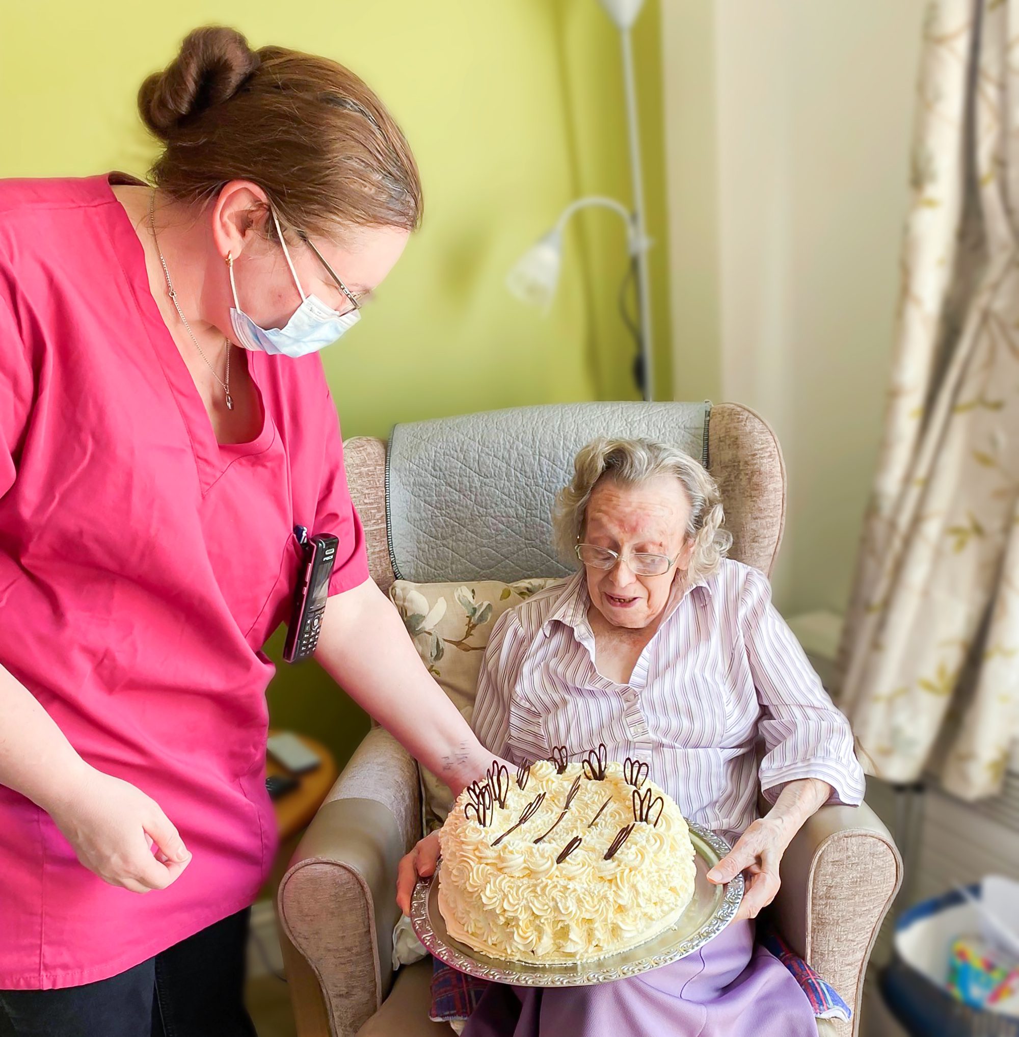 Betty being given her birthday cake by a member of staff at Bernard Sunley care home