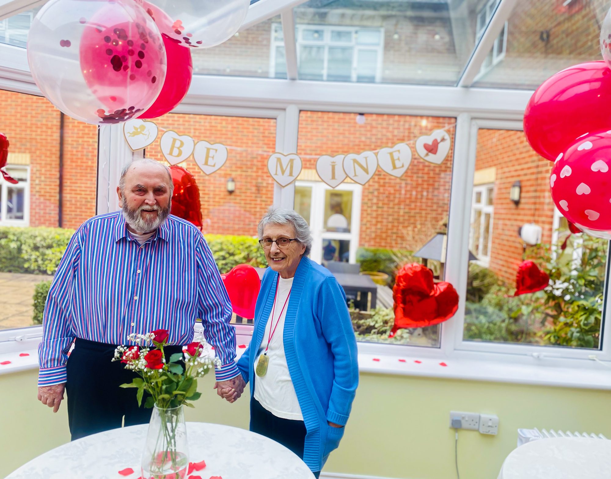 Woking care home couple holding hands with balloons in background. 