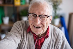 An older man wearing glasses smiling whilst taking a selfie.