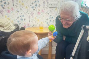 2025 April Highlights: A resident and toddler play with toys together. The resident has a big smile on her face.