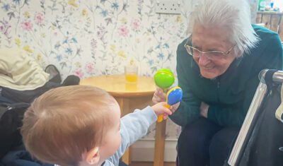 A resident and toddler play with toys together. The resident has a big smile on her face.