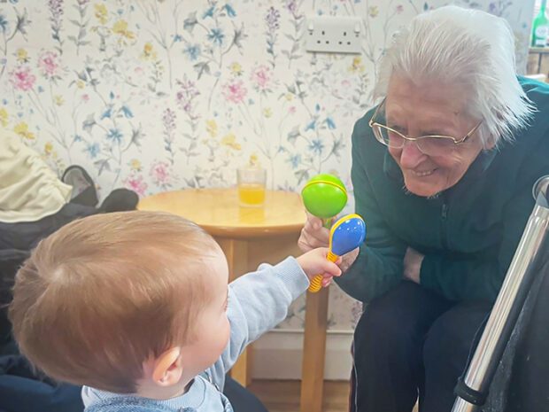 A resident and toddler play with toys together. The resident has a big smile on her face.