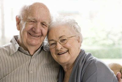 Older Man and Woman Sitting on a couch smiling.